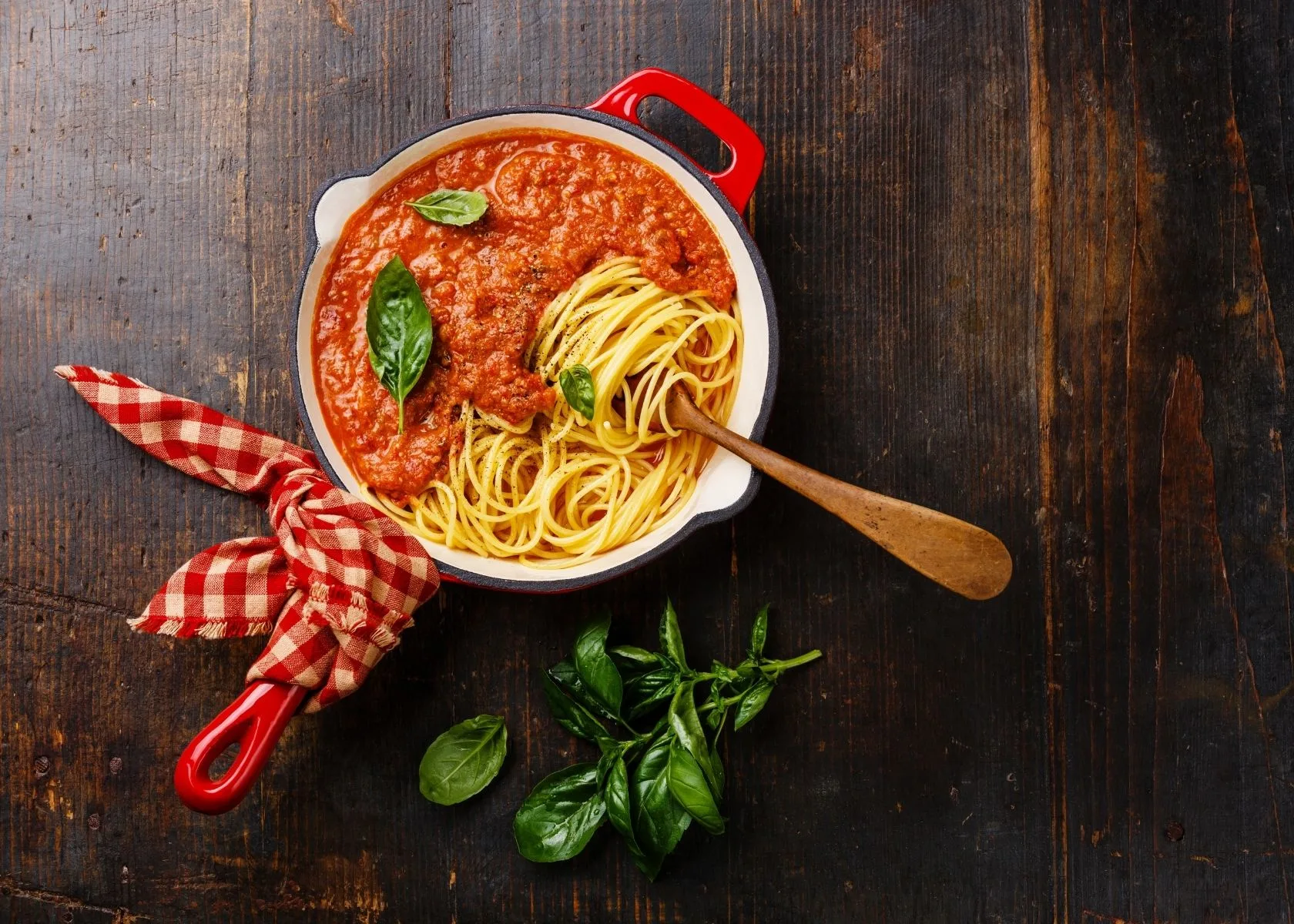 Small pot with spaghetti and pasta sauce on table with fresh basil leaves.