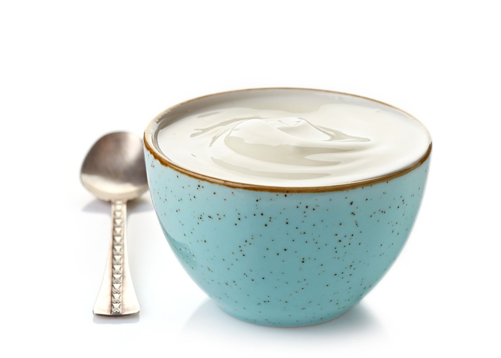 Plain yogurt in blue bowl with brown speckles next to metal spoon.