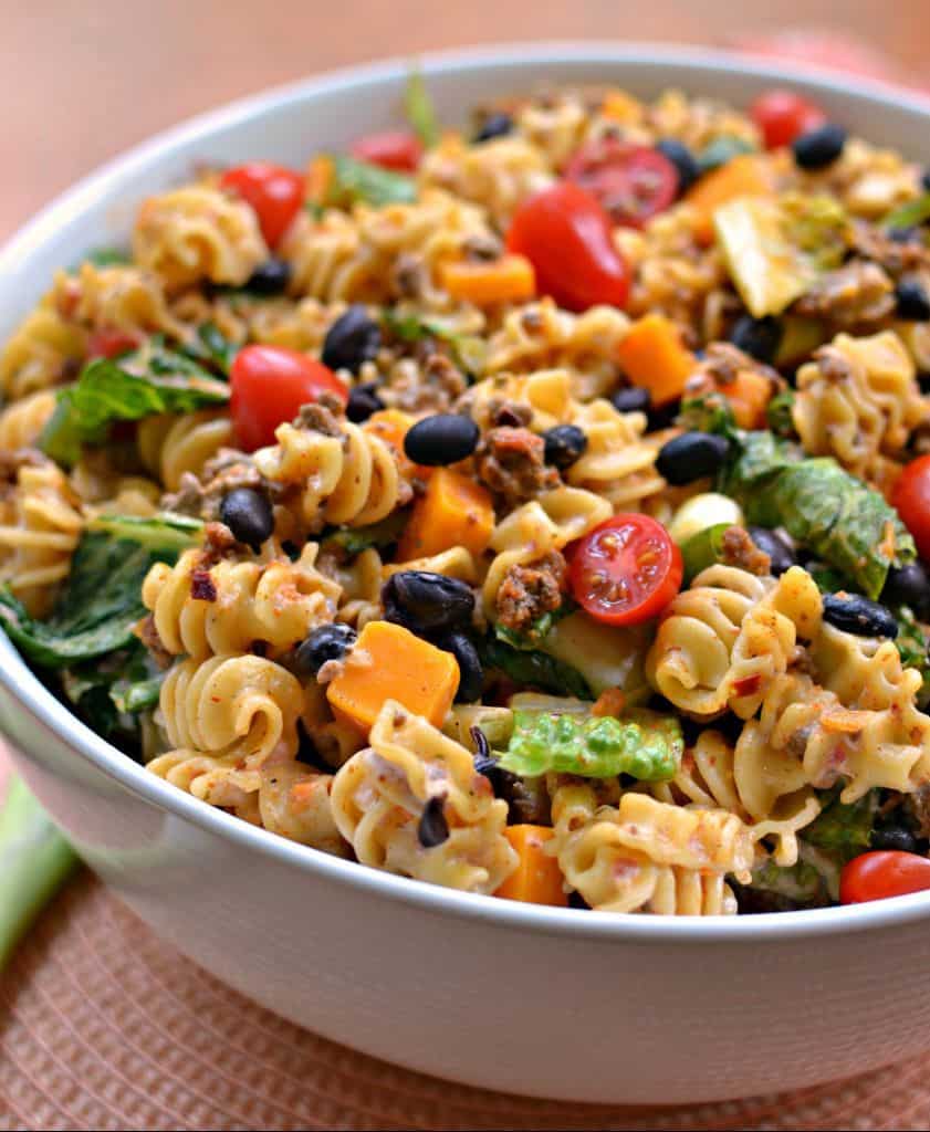 Bowl of taco pasta salad with black beans, cheese, tomatoes and lettuce.