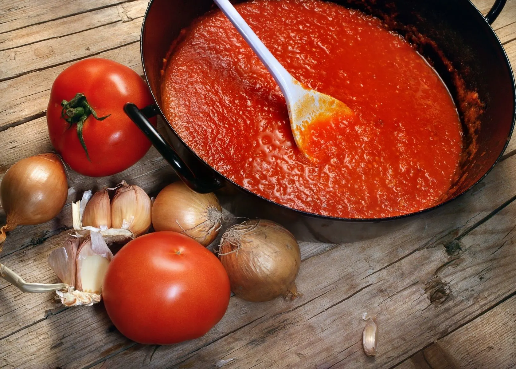Tomato sauce in large cast iron skillet next to fresh tomatoes, garlic and onion.