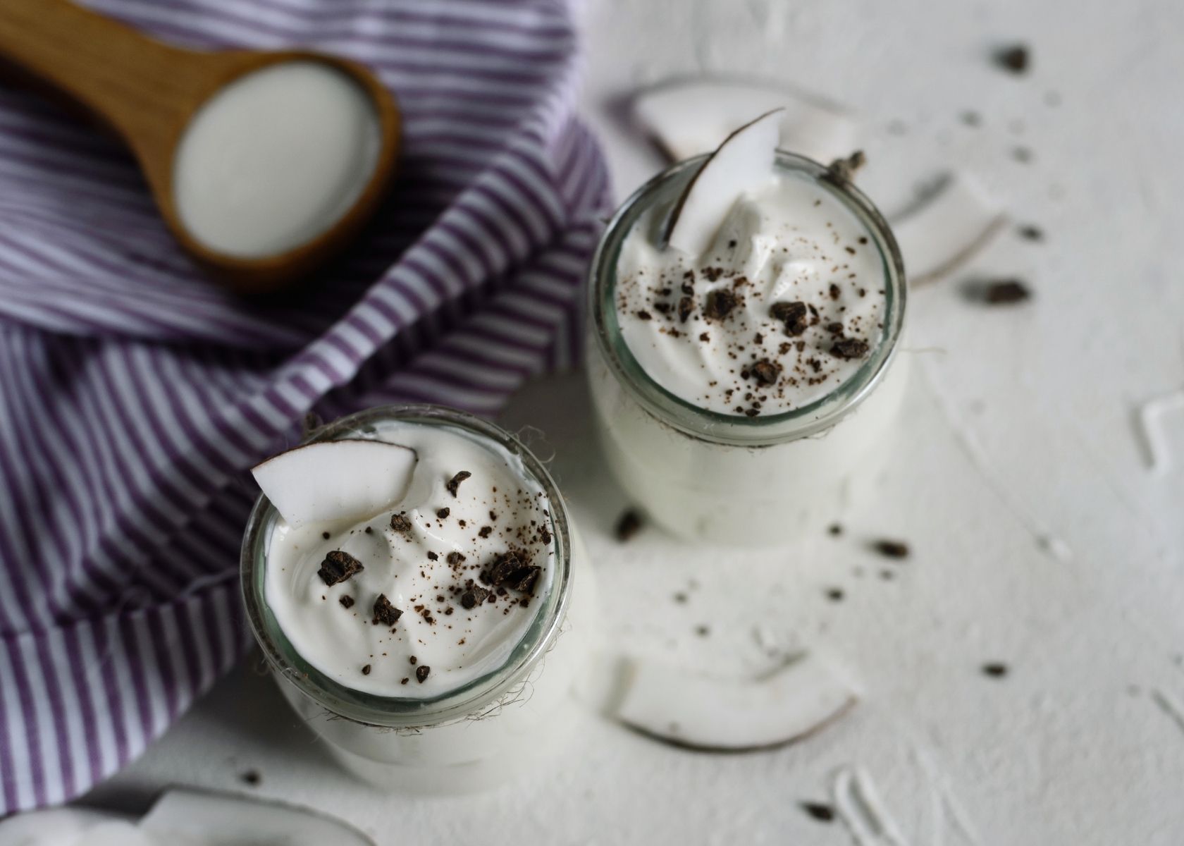 Vegan yogurt in two clear glass jars with coconut and cocoa garnish.