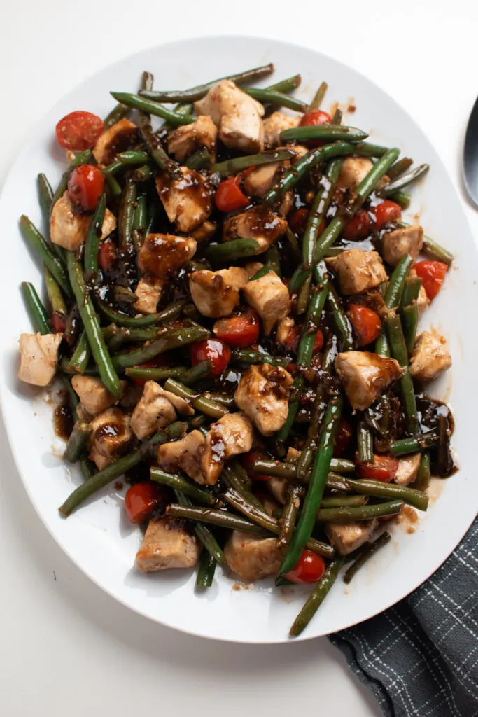 Large white platter of balsamic chicken skillet with green beans and tomatoes.