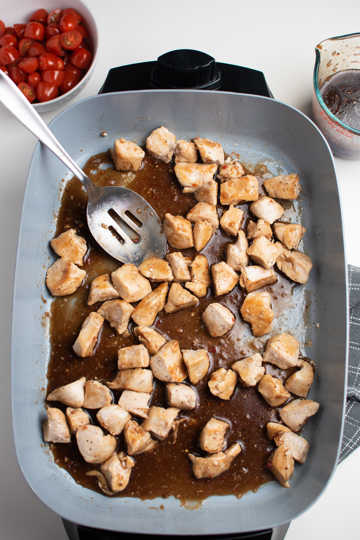 Balsamic sauce, cubed chicken pieces, and slotted spoon in an electric skillet.