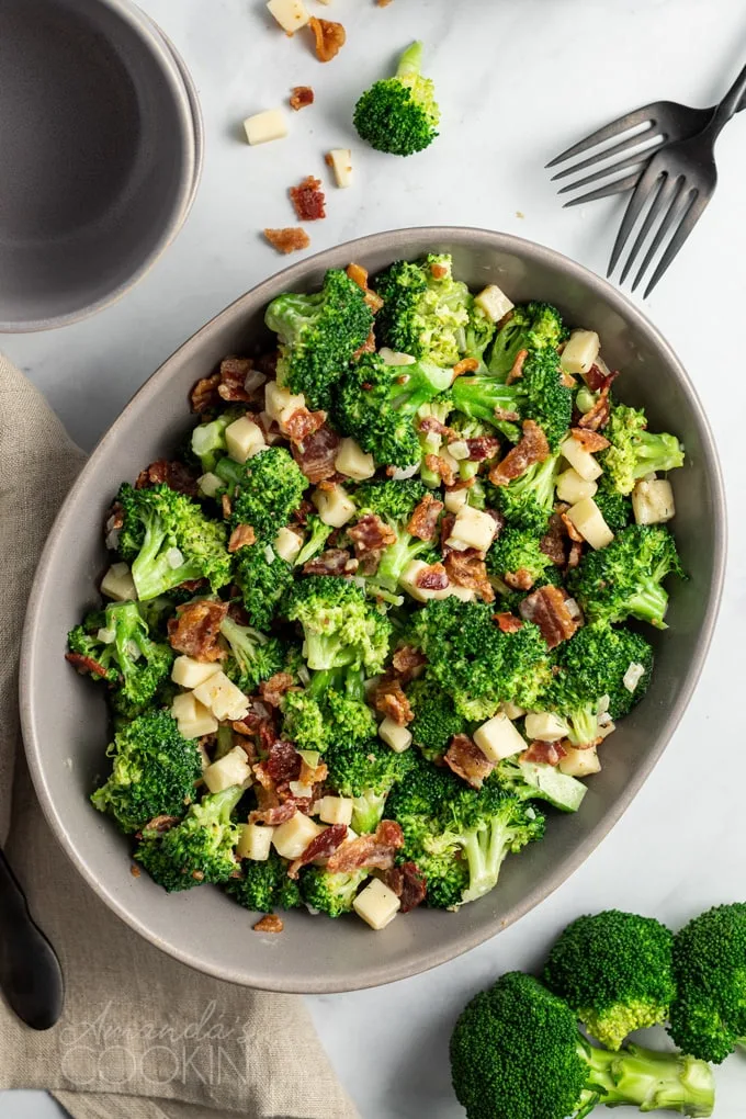 Broccoli salad with bacon and cubed cheese in large gray serving dish.
