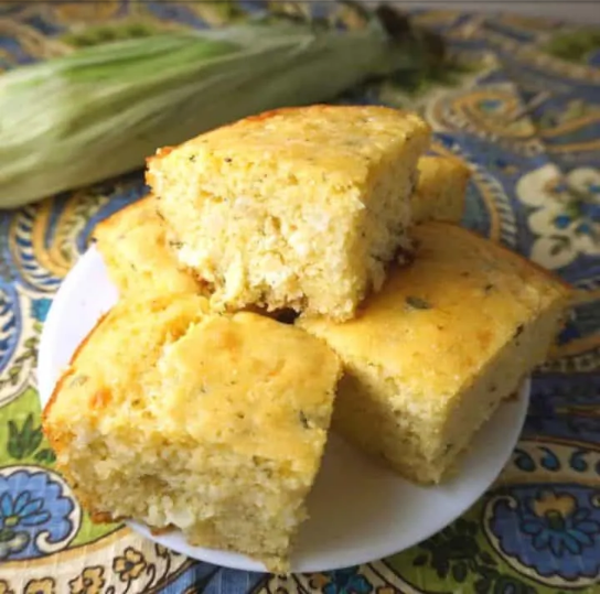 Several pieces of cheddar sage cornbread piled high on white dinner plate.