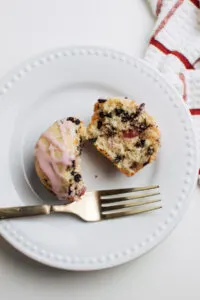 Cherry chocolate chip muffin on white plate with pink glaze and gold fork.