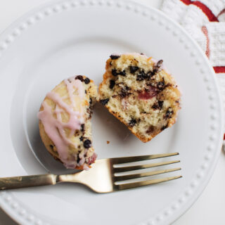Cherry chocolate chip muffin on white plate with pink glaze and gold fork.