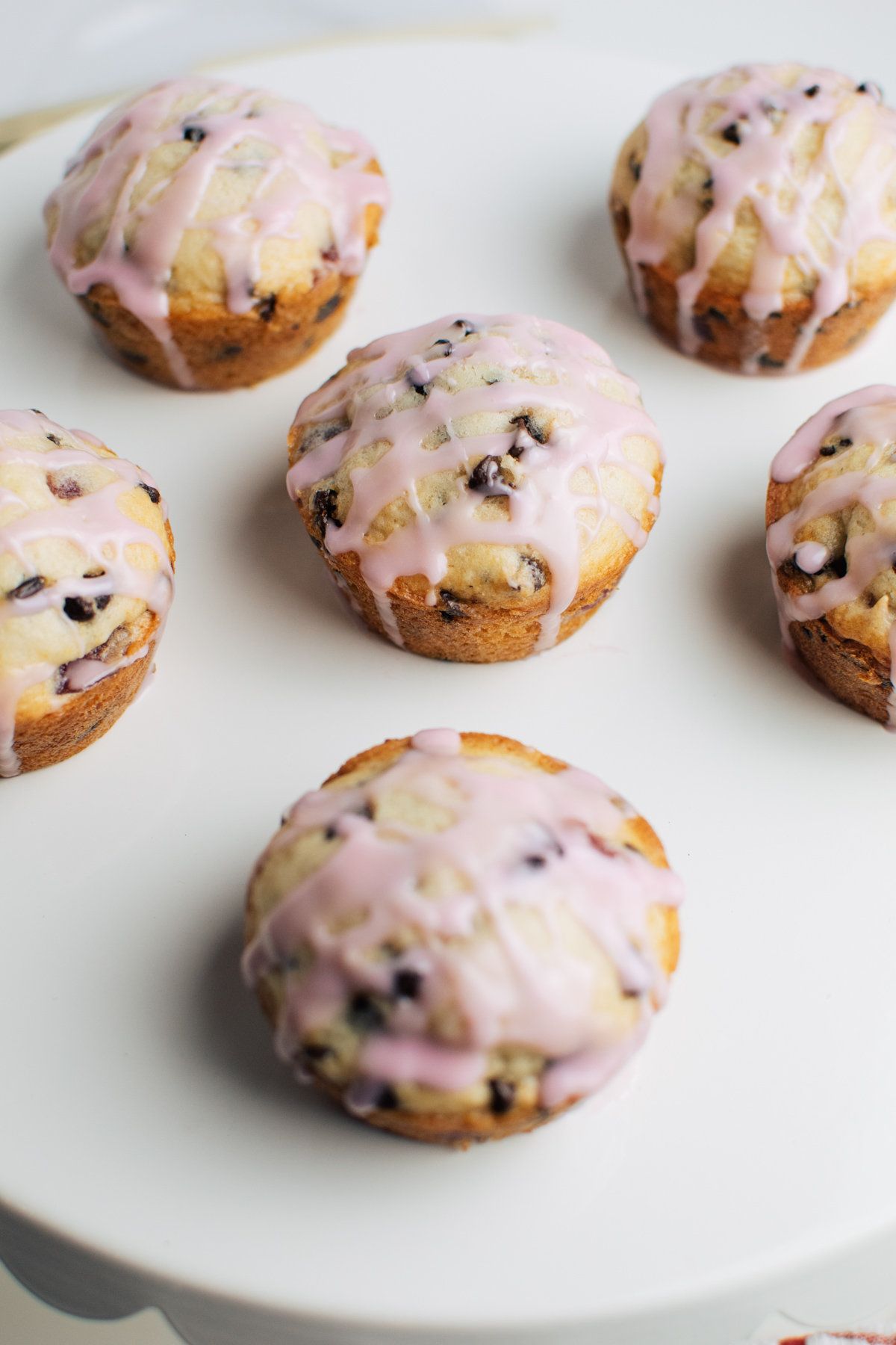 Several cherry chocolate chip muffins with pink glaze on white serving platter.