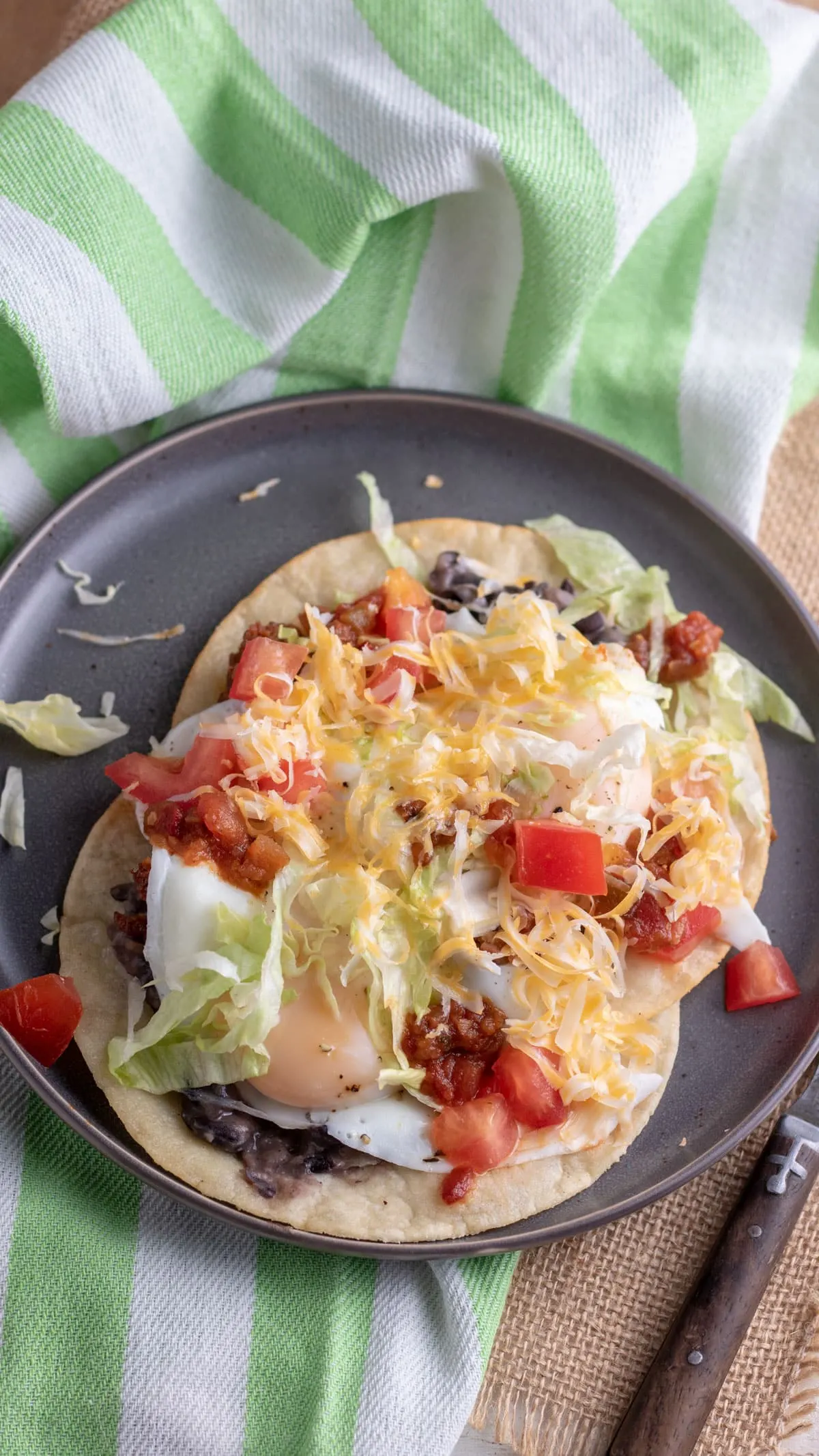 Chorizo huevos rancheros on a blue plate topped with lettuce and tomatoes.