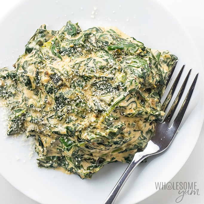 Large mound of creamed spinach with metal fork on large white dinner plate.