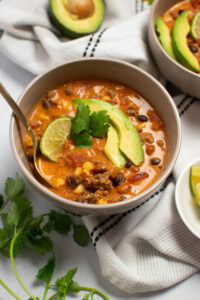 Bowl of creamy taco soup with spoon and cilantro, avocado, and lime garnish.