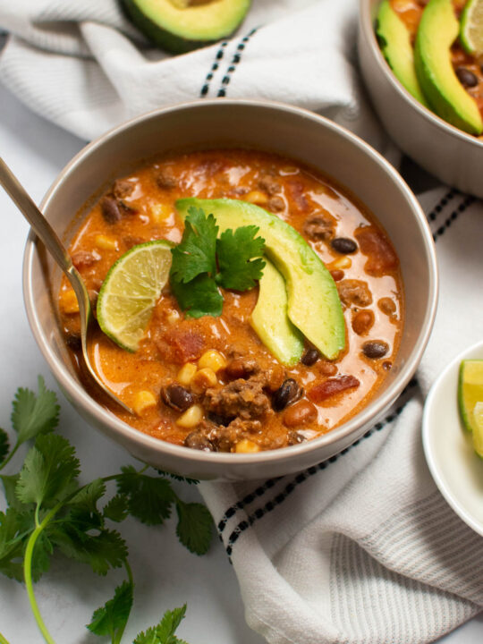 Bowl of creamy taco soup with spoon and cilantro, avocado, and lime garnish.