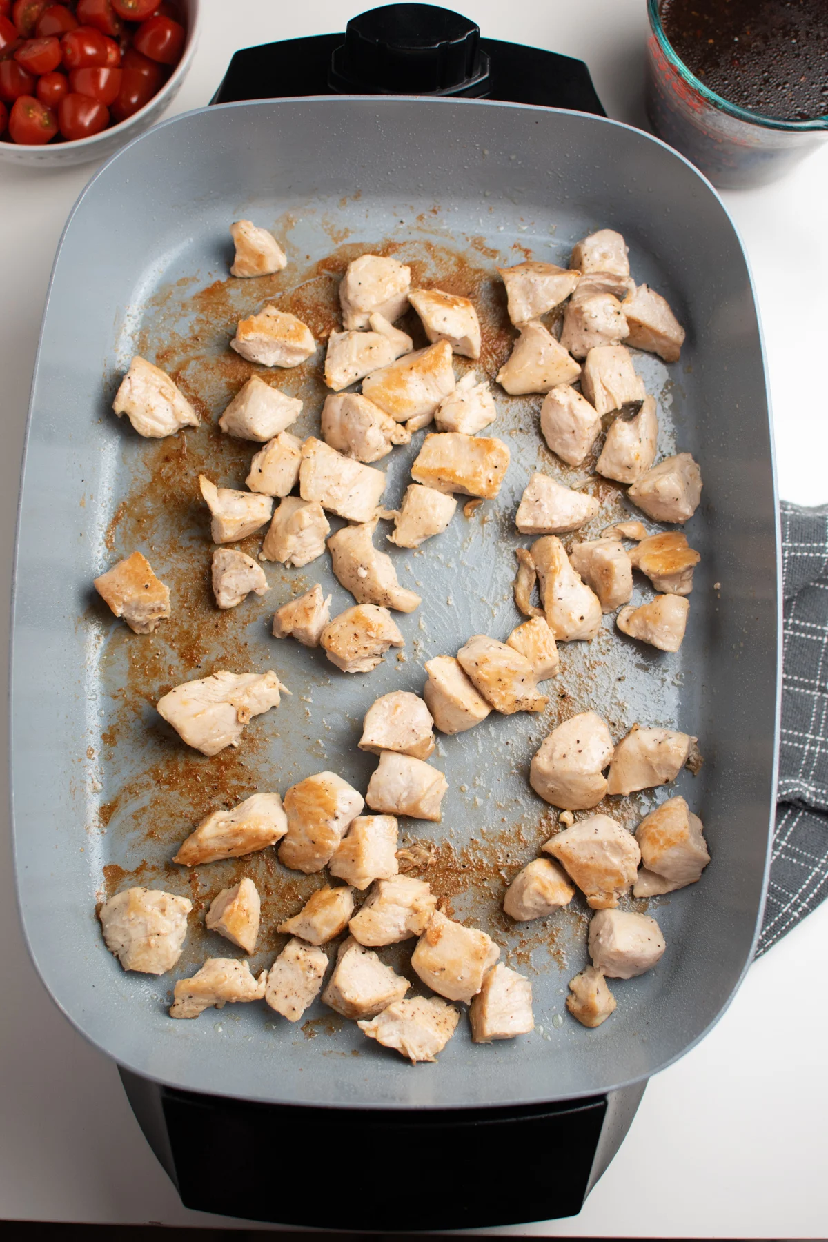 Several pieces of cubed cooked chicken in a skillet on white table.