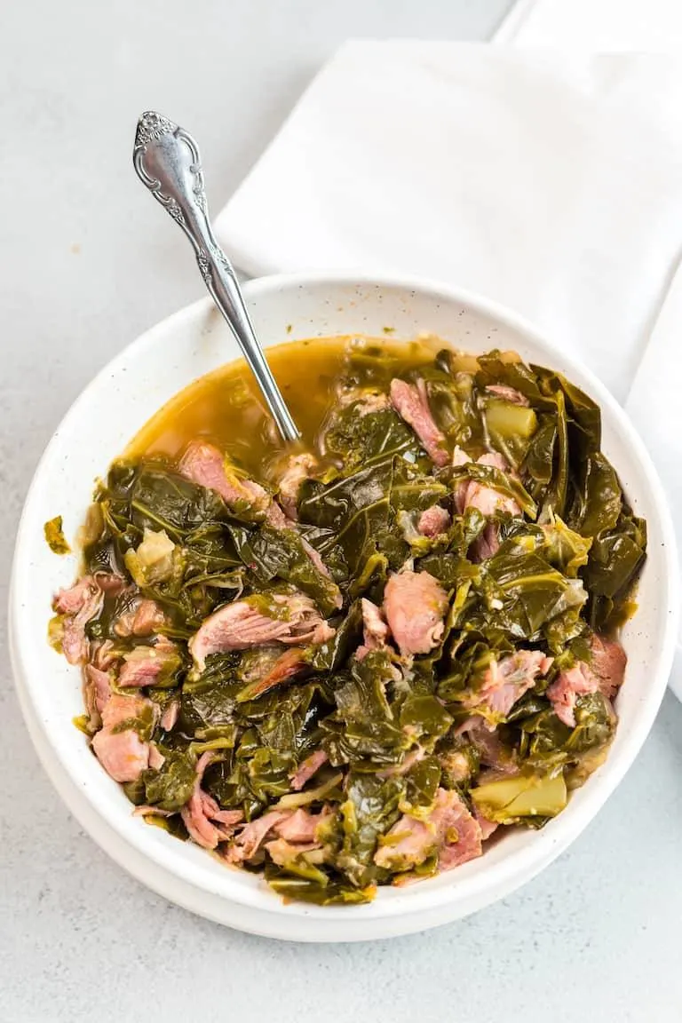 Instant pot collard greens with pieces of smoked ham in large white dinner bowl.