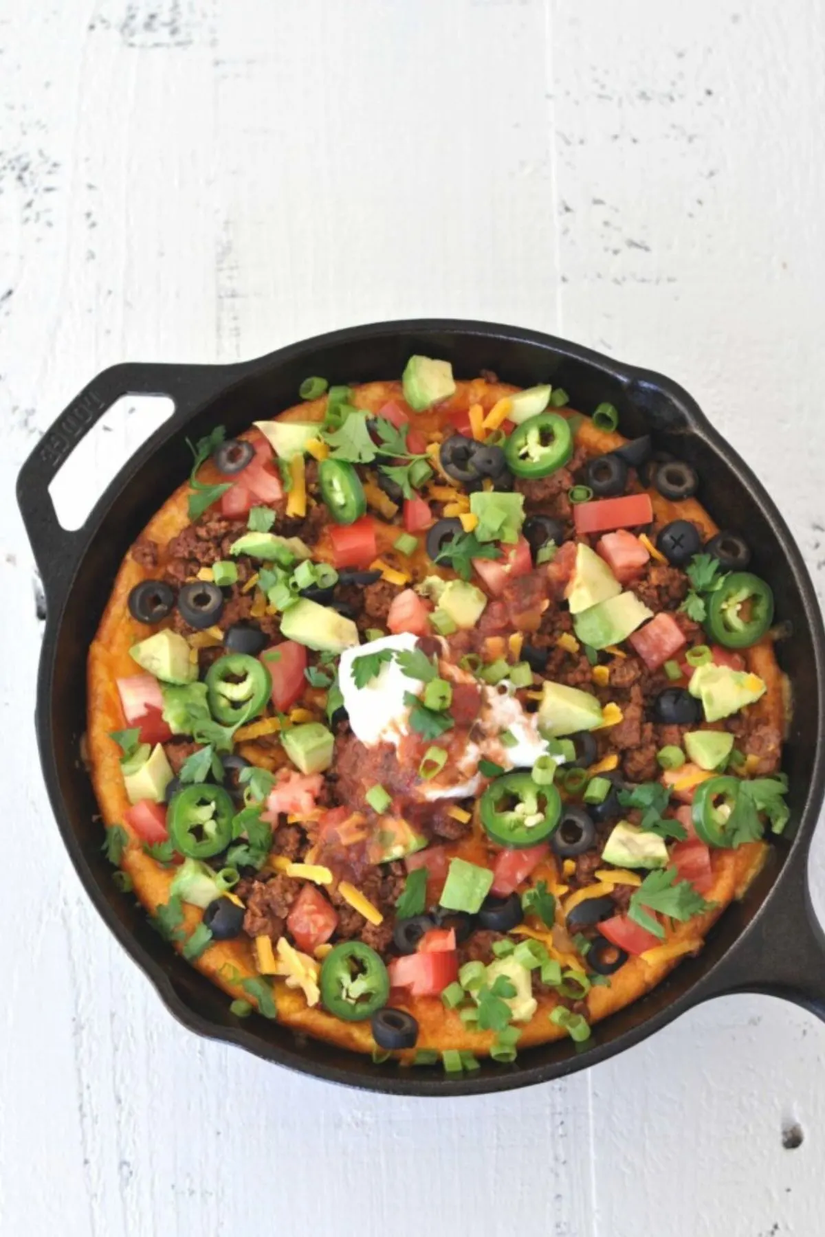 Taco breakfast skillet topped with sour cream, jalapenos and avocado on a white table.