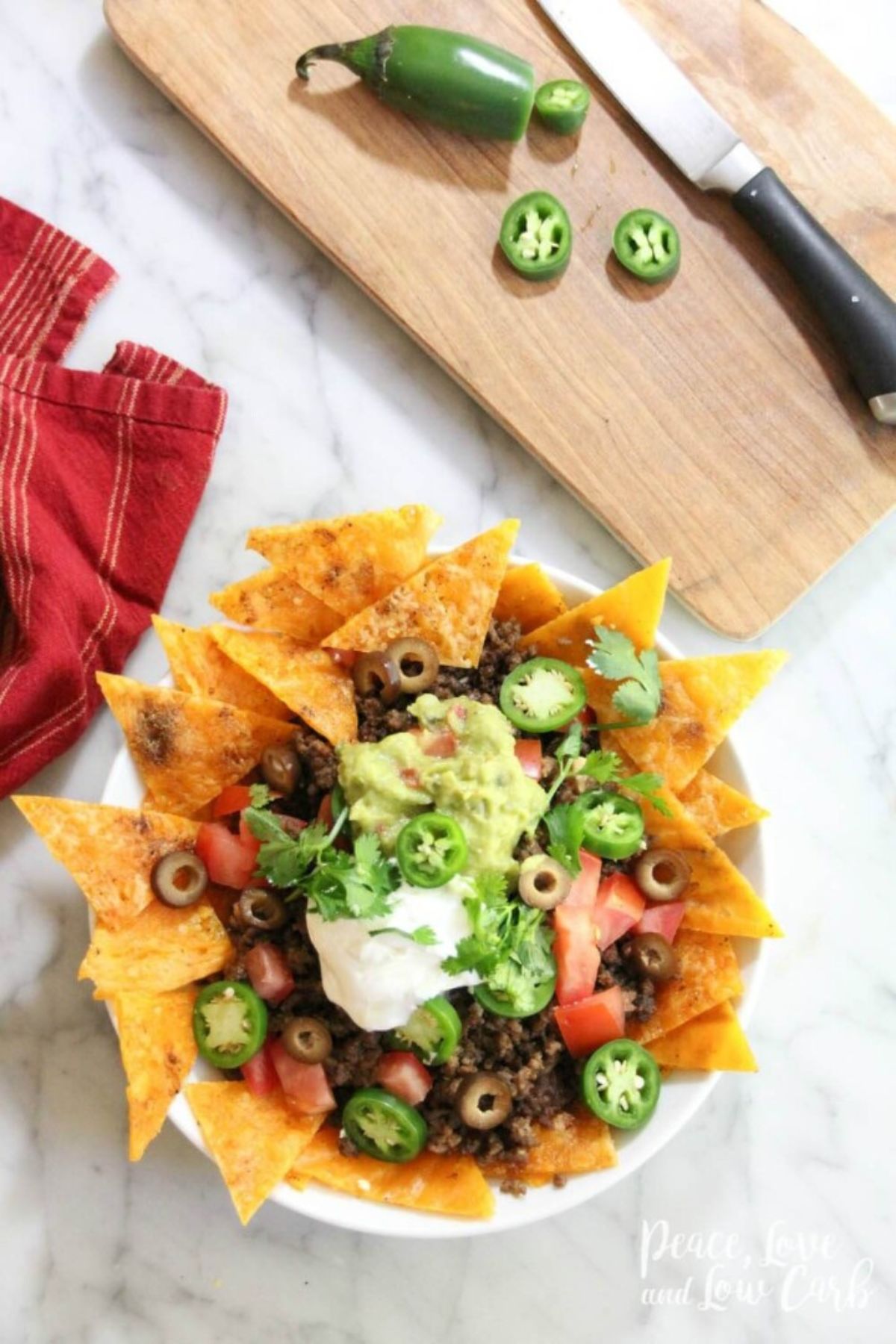 A plate of low carb nachos on a table topped with guacamole and jalapanos.