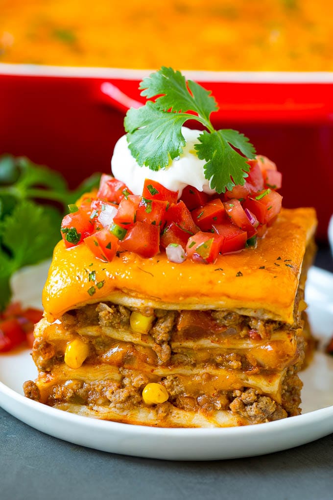 Mexican lasagna on a white plate topped with tomatoes, sour cream and cilantro.