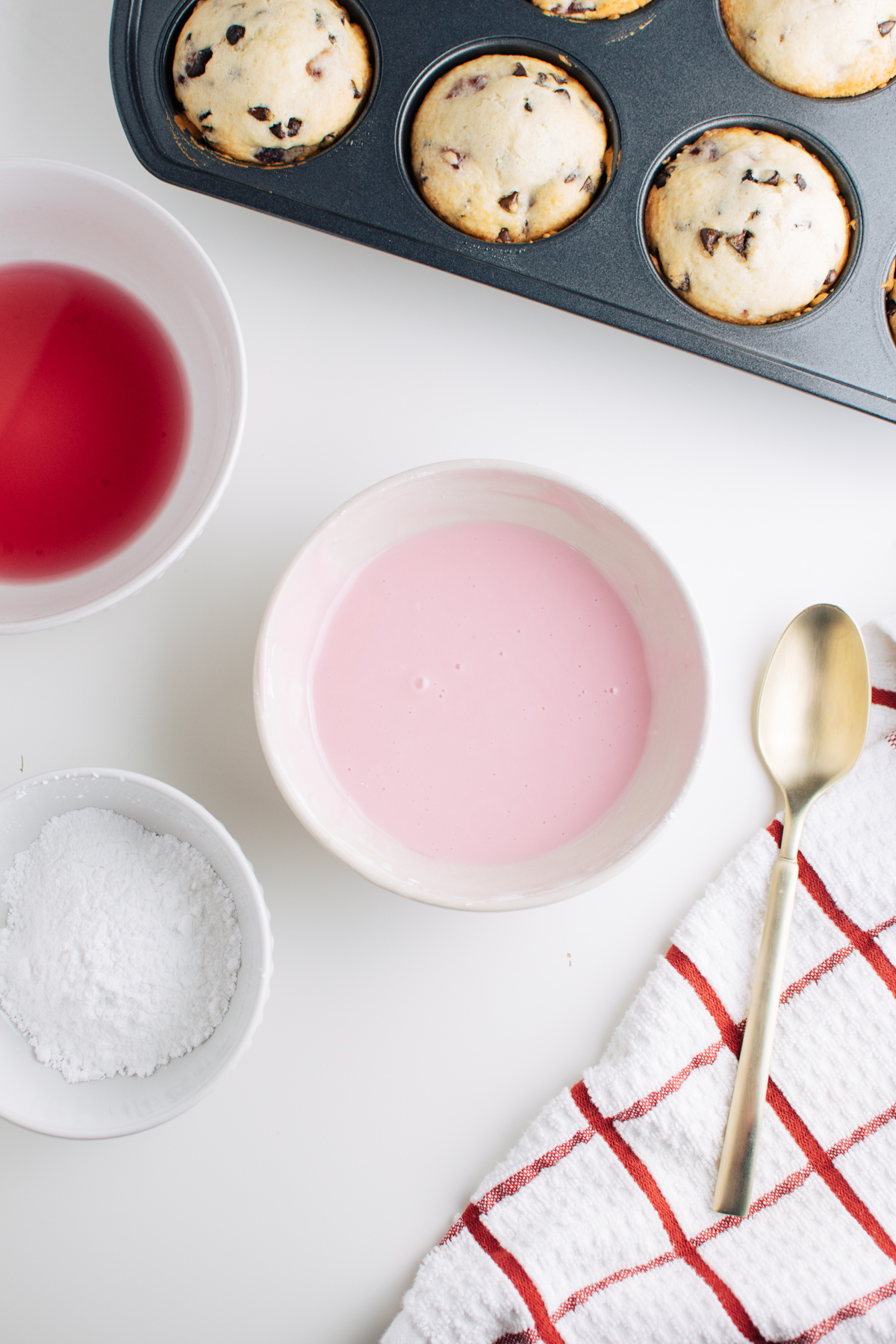 Pink glaze in white bowl next to bowls of powdered sugar and cherry juice.