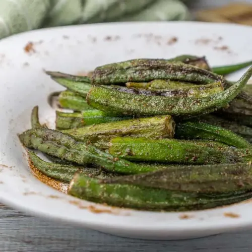 Large pile of charred and roasted Cajun okra on large white serving dish.