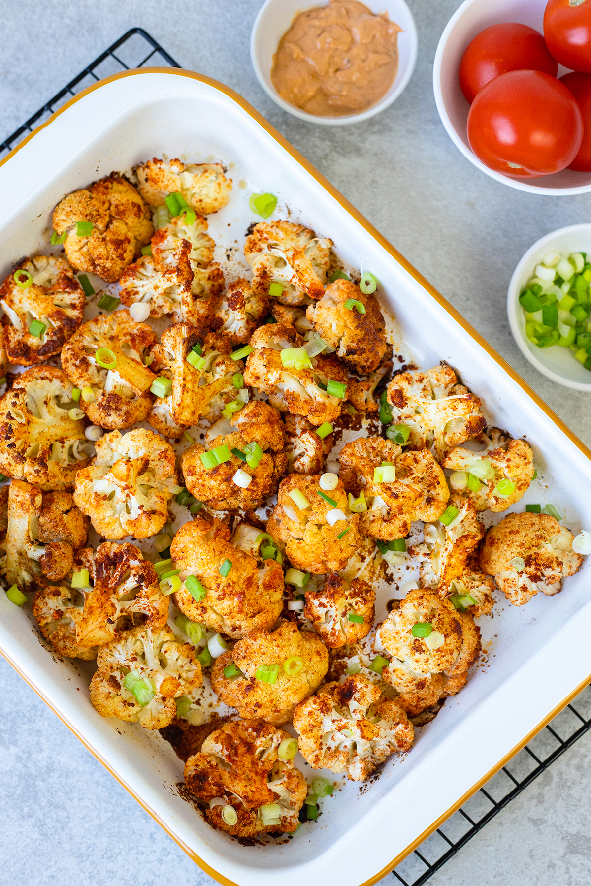 Spicy roasted cauliflower topped with green onion garnish in white casserole dish.