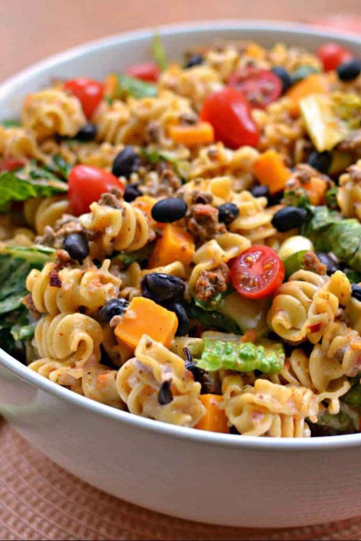 Bowl of taco pasta salad with black beans, cheese, tomatoes and lettuce.
