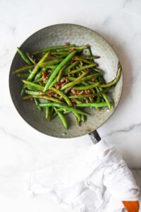 Balsamic green beans with bacon in decorate gray skillet on marble counter.