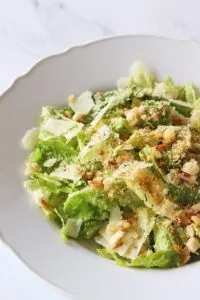 Large breadcrumb Caesar salad in white serving bowl with shavings of cheese.