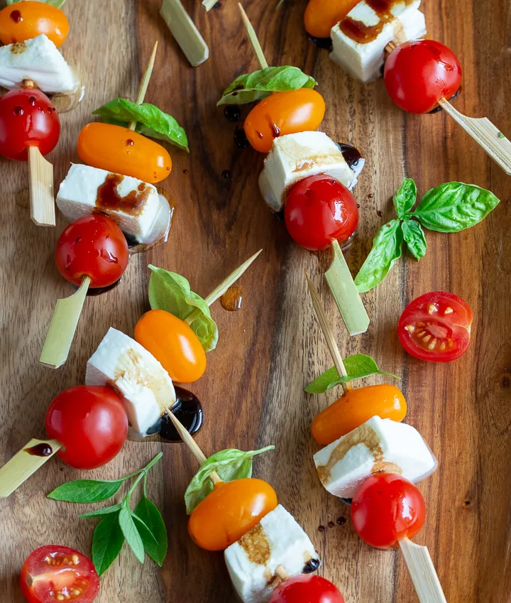 Caprese salad skewers with red and orange grape tomatoes on wooden cutting board.