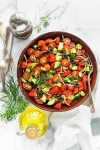 Large bowl of cucumber and tomato salad with red onion and black olives.
