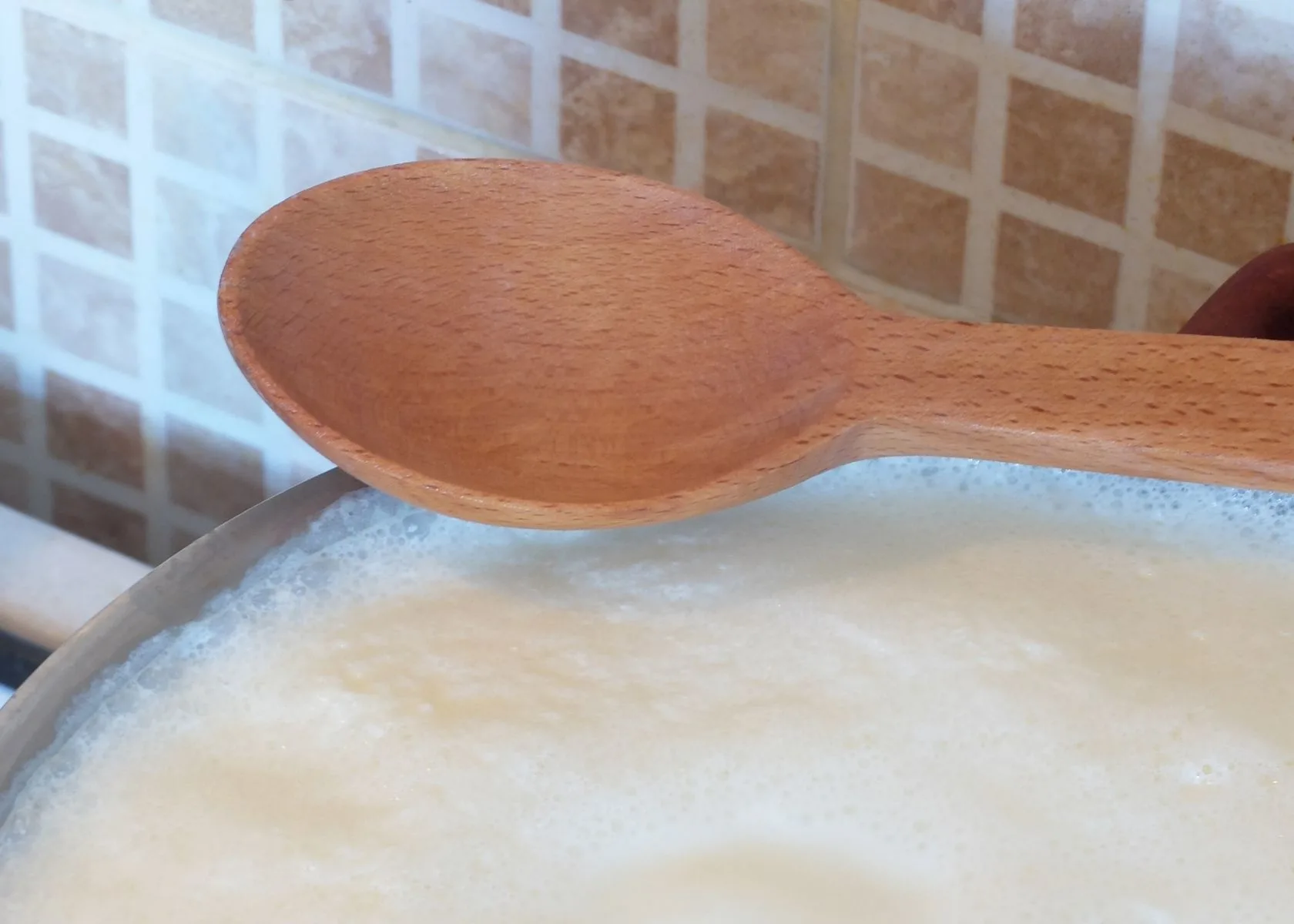 Homemade evaporated milk boiling in large stock pot with wooden spoon on top.