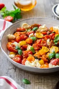 Roasted cherry tomato salad with basil leaves and goat cheese in bowl.