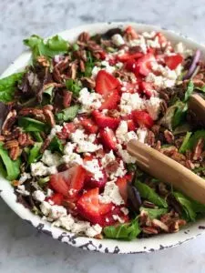 Large white bowl of strawberry pecan salad with feta and wooden salad spoons.