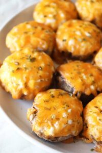 Air fryer stuffed mushrooms topped with green garnish and cheese on plate.