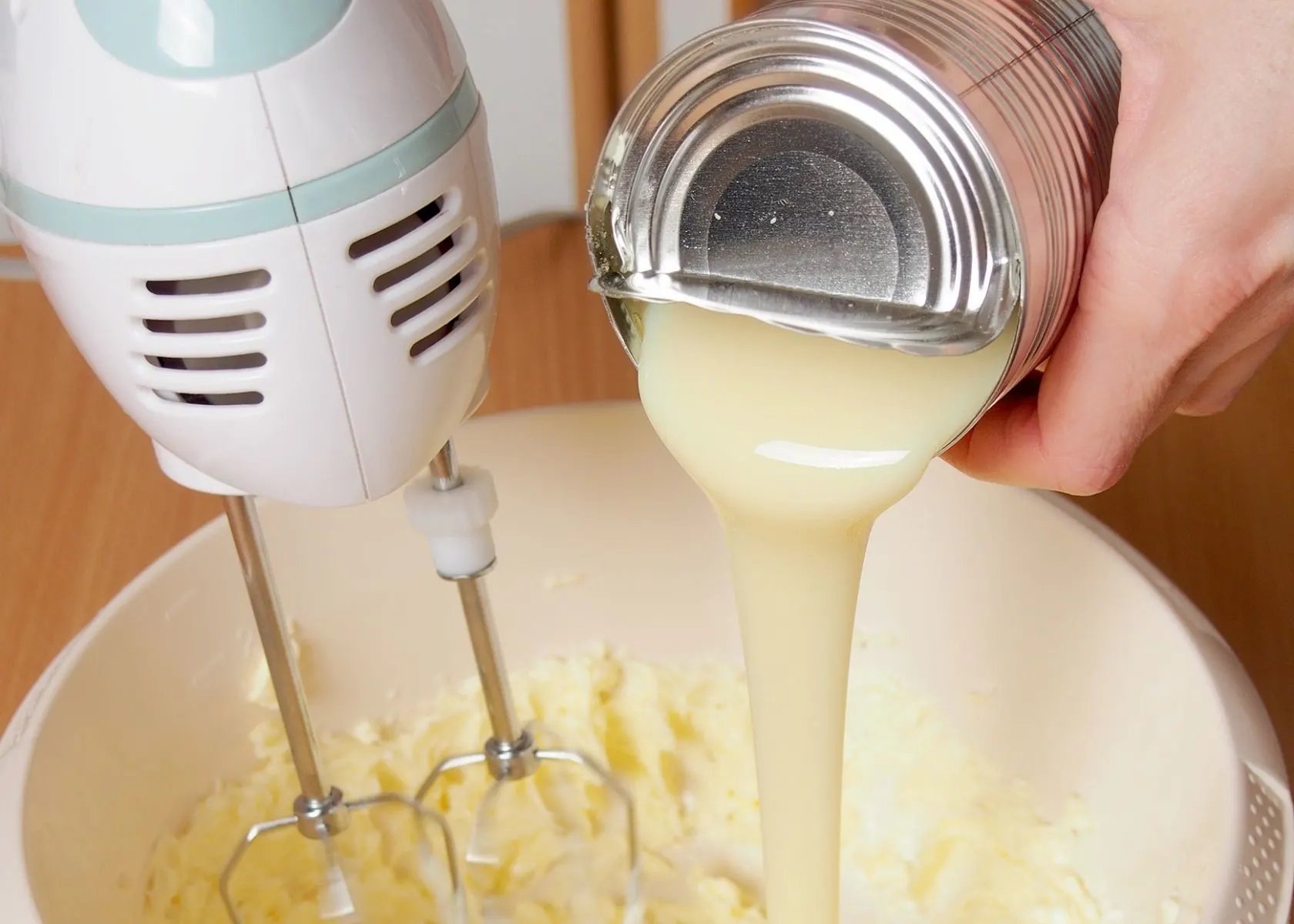 Sweetened condensed milk is poured into mixing bowl and blended with baking ingredients.