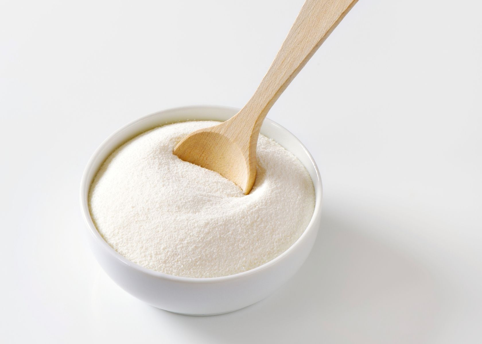 Large mound of xanthan gum powder in white bowl with wooden spoon.