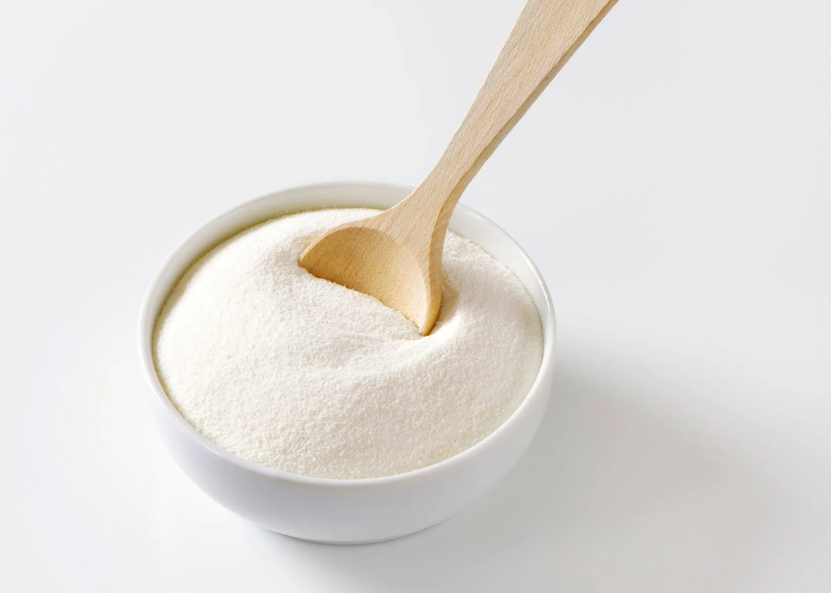 Large mound of xanthan gum powder in white bowl with wooden spoon.