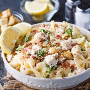 Chicken Caesar pasta salad with bacon bits and lemon in white bowl.