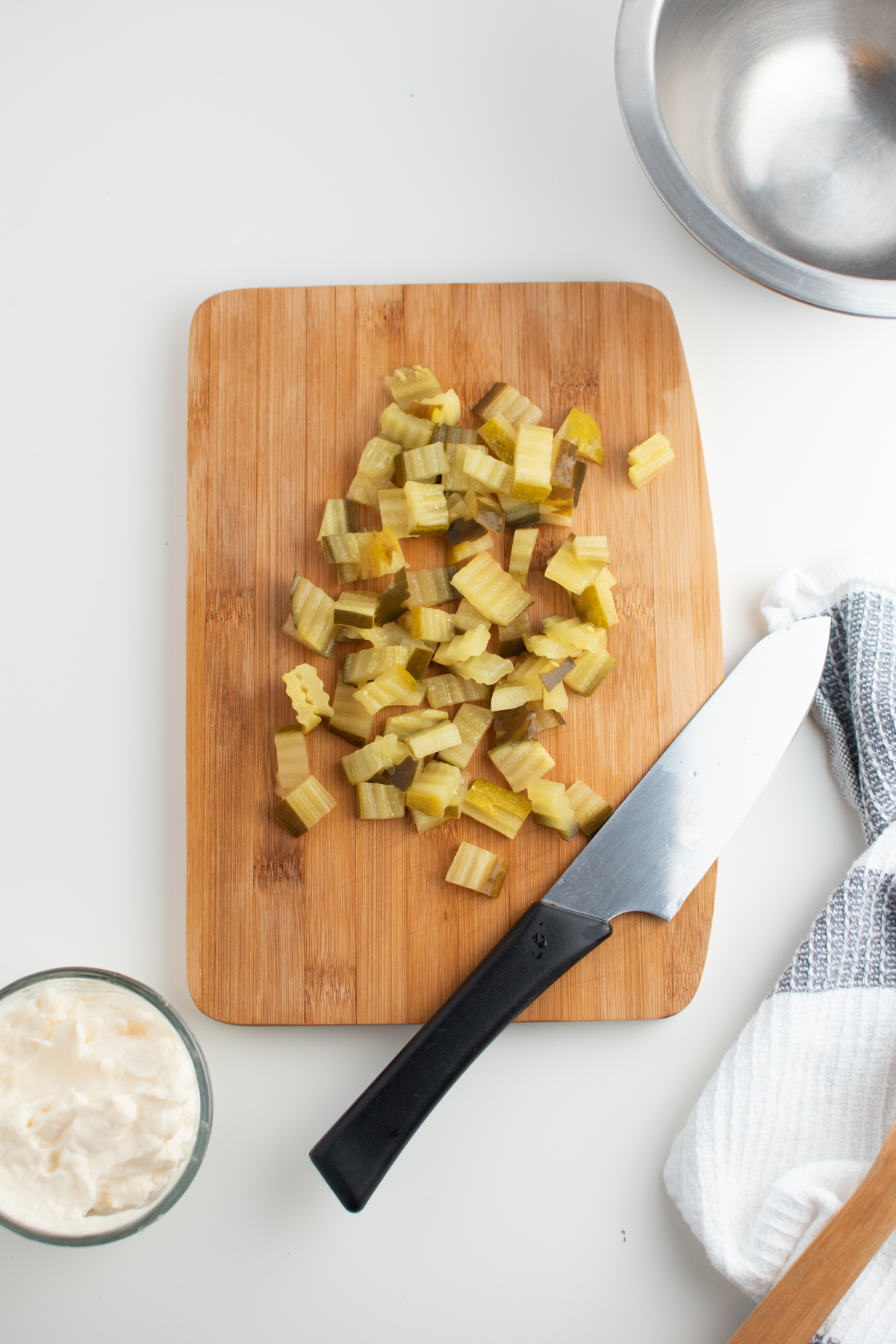Several chopped pickles on wooden cutting board with knife and kitchen towel.