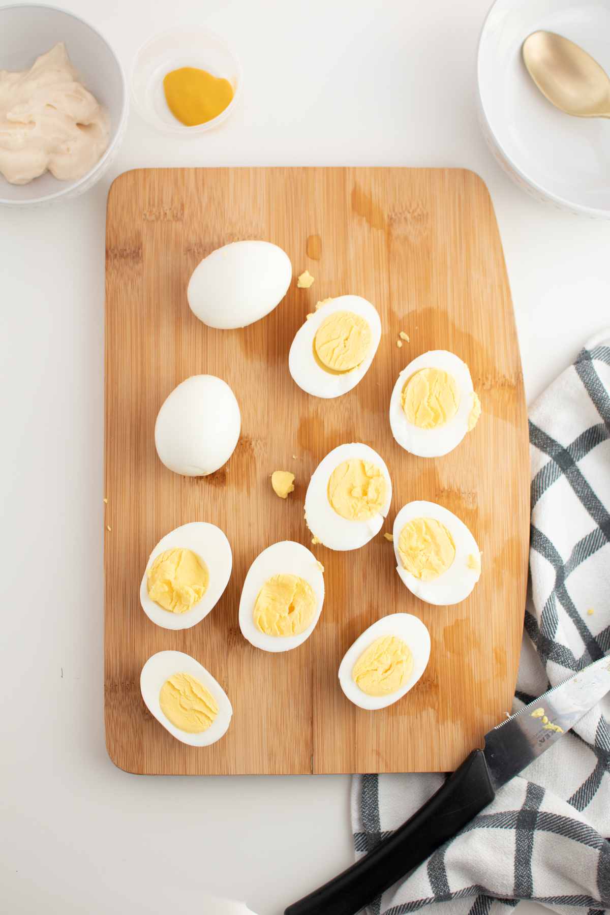 Hard boiled eggs cut in half on wooden cutting board next to prep bowls.