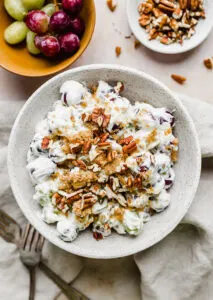 White bowl with brown and tan flecks filled with grape salad on table.