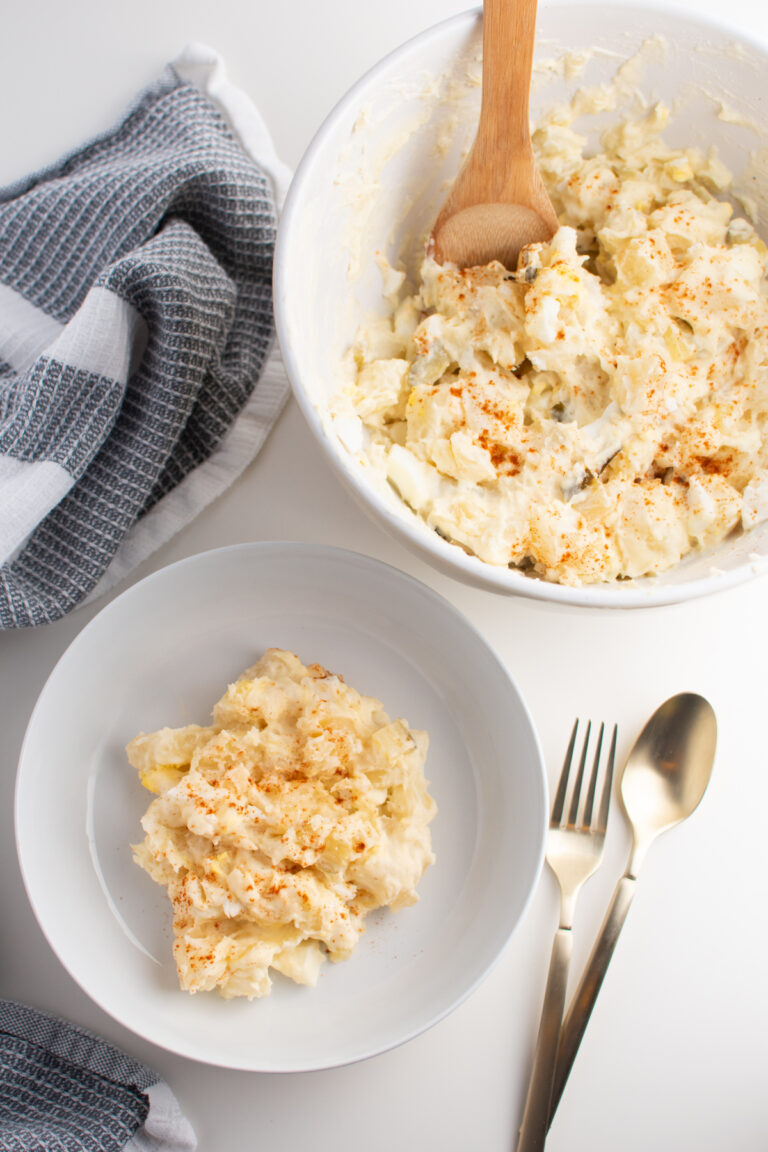 Instant Pot potato salad in serving bowl and dinner bowl by kitchen towel.