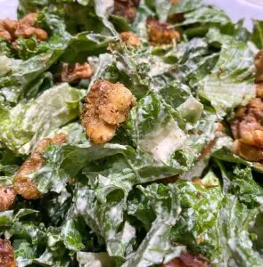 Close up of kale Romain Caesar salad with walnut croutons in large white bowl.