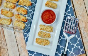 Mozzarella cheese sticks on cooling rack and white platter with marinara sauce.