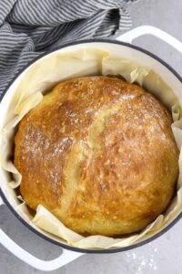 Loaf of no knead artisan bread in white Dutch oven pot with parchment paper.
