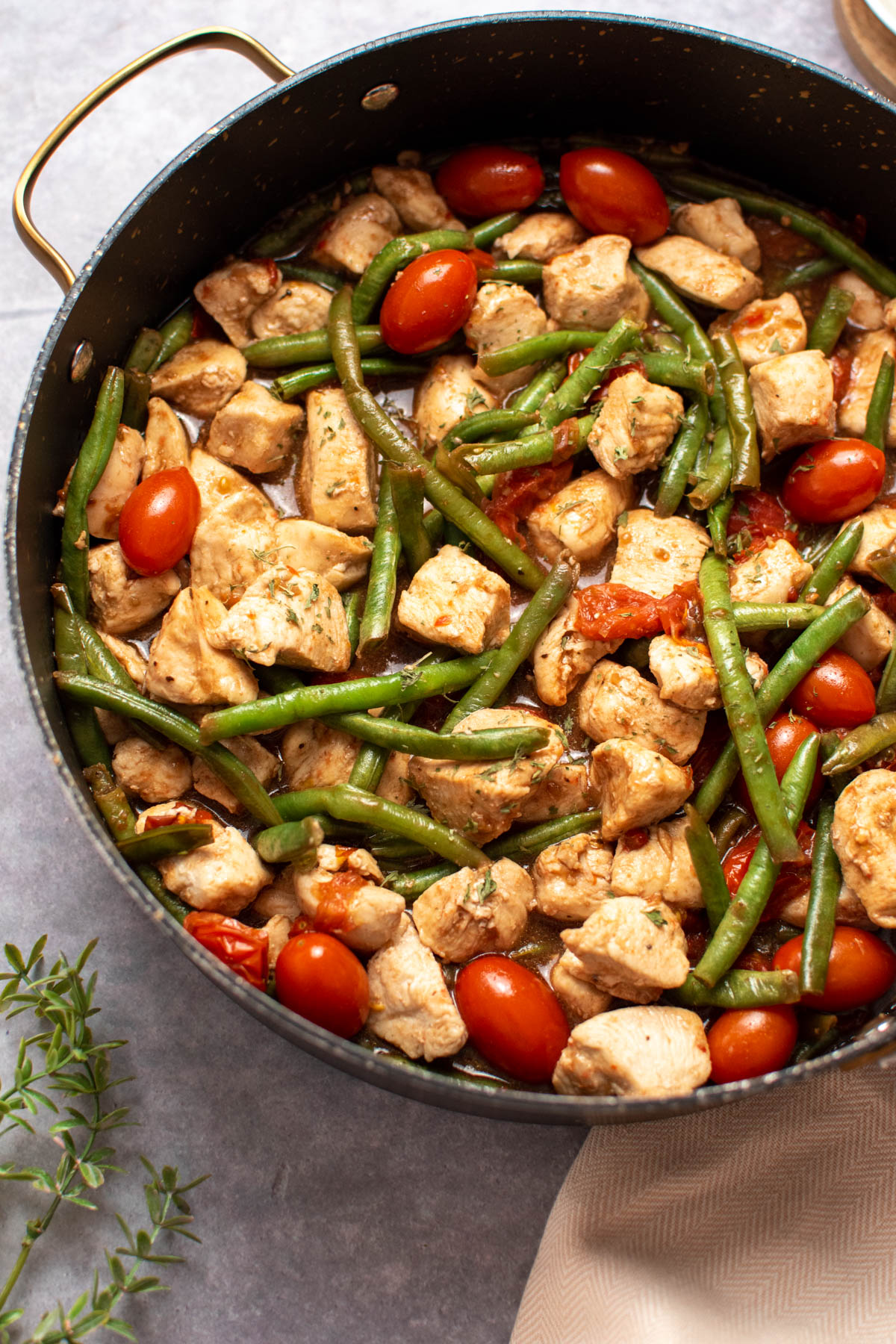 Large black skillet with balsamic chicken, tomatoes, and green beans on dark tabletop.