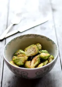 Bowl of oven roasted brussels sprouts in white dinner bowl with green pattern on table.