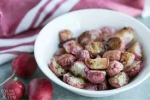 Bowl of oven roasted purple radishes next to red and white kitchen towel.