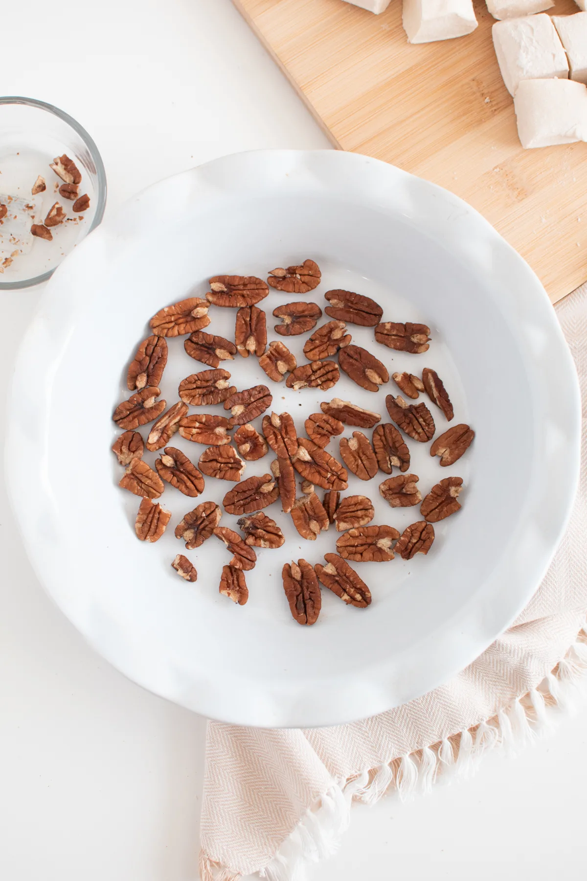 Pecan halves spread out on the bottom of white, decorative pie pan.