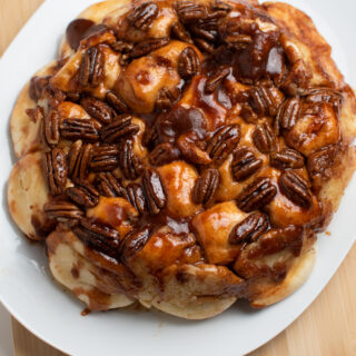 Fresh sticky buns on large white serving platter topped with caramelized pecans.