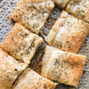 Pieces of square stuffed cheesy bread with green garnish on parchment paper.